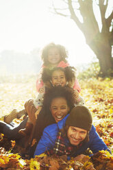 Portrait smiling young family laying on top of each other in sunny autumn leaves - CAIF05440