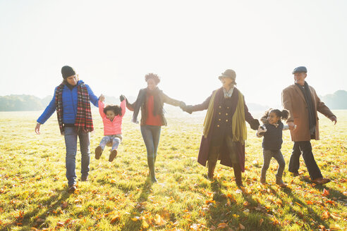 Verspielte Mehrgenerationenfamilie beim Spaziergang im sonnigen Herbstgras des Parks - CAIF05444