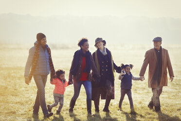 Mehrgenerationenfamilie, die sich an den Händen hält und im sonnigen Herbstgras spazieren geht - CAIF05448