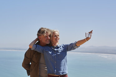 Affectionate senior couple taking selfie overlooking sunny ocean view - CAIF05454