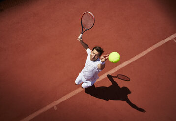 Draufsicht auf einen jungen männlichen Tennisspieler, der auf einem sonnigen Tennisplatz den Ball aufschlägt - CAIF05461