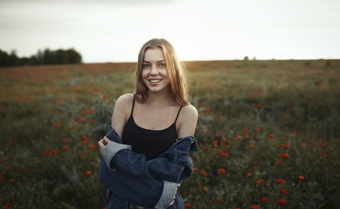 Porträt lächelnde junge Frau in ländlichem Feld mit Wildblumen, lizenzfreies Stockfoto