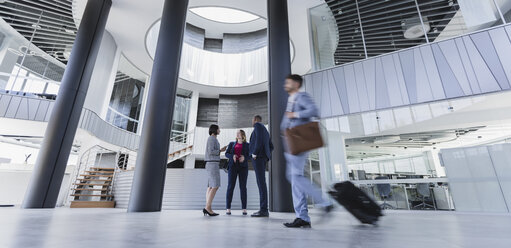 Geschäftsleute unterhalten sich und ziehen Koffer in einer architektonischen, modernen Bürolobby - CAIF05501