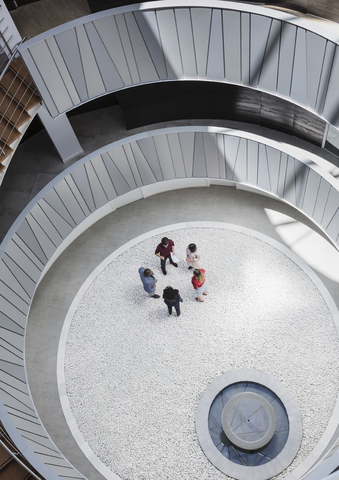 Blick von oben auf Geschäftsleute, die sich in einem runden, modernen Büro-Atrium-Hof unterhalten, lizenzfreies Stockfoto