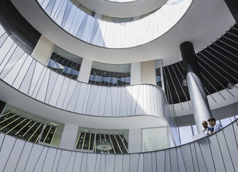Geschäftsleute besprechen Papierkram auf einem architektonischen, modernen Büro-Atrium-Balkon - CAIF05520