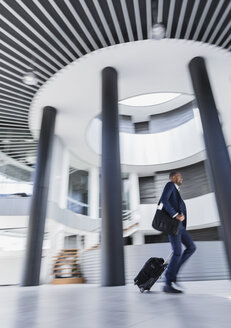 Geschäftsmann eilt, zieht Koffer in architektonischer, moderner Bürolobby - CAIF05525