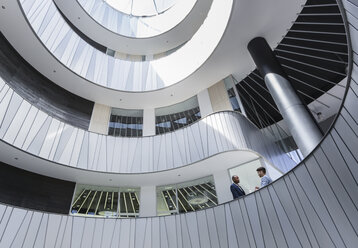 Geschäftsleute im Gespräch auf einem architektonischen, modernen Büro-Atrium-Balkon - CAIF05527