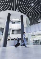 Geschäftsmann im Gehen, der einen Koffer in einer architektonischen, modernen Bürolobby zieht - CAIF05533