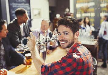 Porträt eines lächelnden, selbstbewussten männlichen Barkeepers, der an einer Bar Bier serviert - CAIF05544