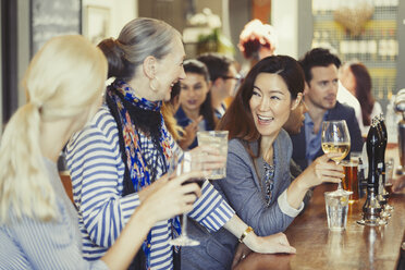 Lächelnde Freundinnen trinken Wein an einer Bar - CAIF05551