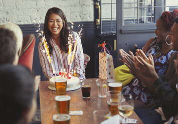 Friends clapping for happy woman with fireworks birthday cake at restaurant table - CAIF05559