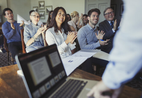 Lächelnde Geschäftsleute, die für einen Geschäftsmann klatschen, der eine Konferenzpräsentation am Laptop leitet - CAIF05564