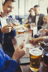 Woman holding aces four of a kind playing poker and drinking beer with friends at bar - CAIF05576
