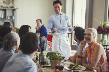 Lächelnder Kellner, der Freunden am Tisch im Restaurant das Essen serviert - CAIF05577