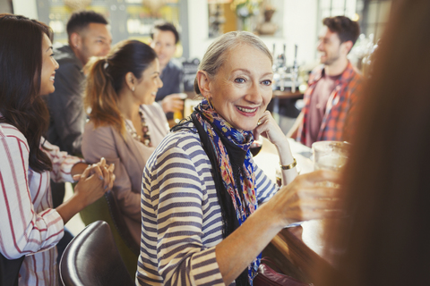 Lächelnde ältere Frau trinkt und unterhält sich mit einem Freund an einer Bar, lizenzfreies Stockfoto