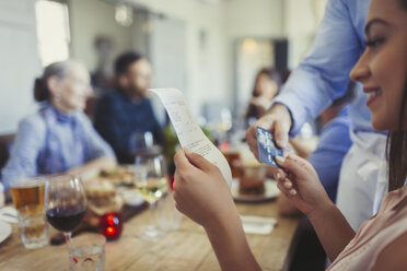 Woman reviewing bill and paying waiter with credit card at restaurant table - CAIF05581