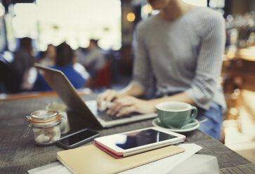 Kreative Geschäftsfrau arbeitet an einem Laptop hinter einem digitalen Tablet in einem Café - CAIF05604