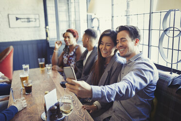 Smiling couple taking selfie with camera phone at table in bar - CAIF05606