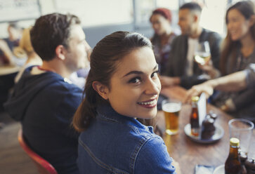 Portrait lächelnde Frau trinkt Bier mit Freunden am Tisch in einer Bar - CAIF05614