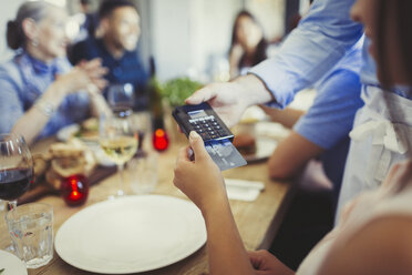 Woman with credit card paying waiter, using credit card reader at restaurant table - CAIF05619