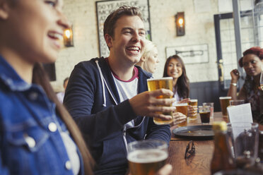 Smiling man drinking beer with friends at table in bar - CAIF05620