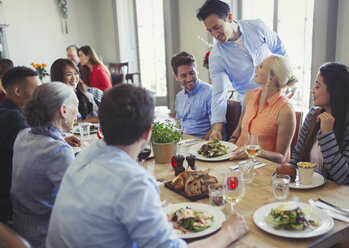 Waiter serving food to friends dining at restaurant table - CAIF05621