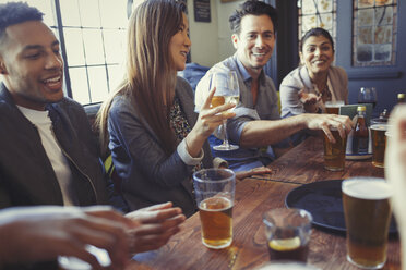 Friends drinking beer and wine and talking at table in bar - CAIF05622