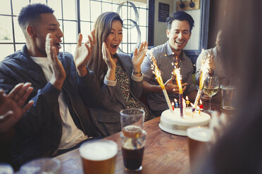 Friends cheering for woman celebrating birthday with fireworks cake at table in bar - CAIF05626