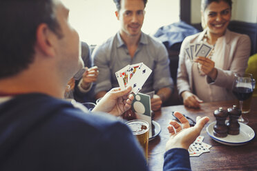 Friends playing poker and drinking beer and wine at table in bar - CAIF05634