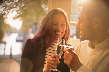 Smiling, romantic couple toasting champagne glasses in restaurant - CAIF05649