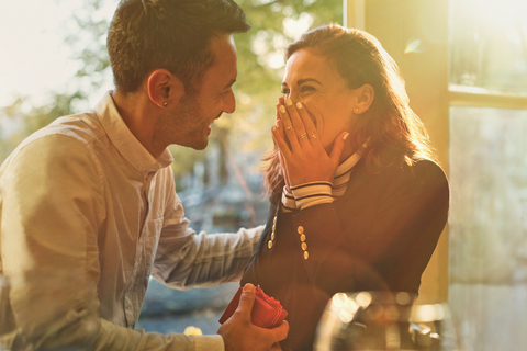 Boyfriend proposing to surprised, happy girlfriend in cafe stock photo