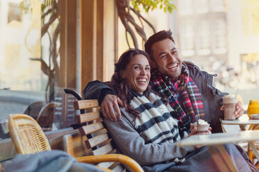 Portrait laughing young couple drinking milkshakes at urban sidewalk cafe - CAIF05660