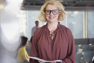Porträt einer lächelnden, selbstbewussten Geschäftsfrau mit Papierkram im Büro - CAIF05686
