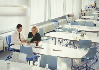Geschäftsmann und Geschäftsfrau besprechen Papierkram am Tisch in einem gemeinsamen Arbeitsbereich - CAIF05705