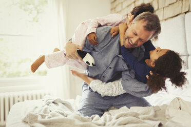 Multiethnische Töchter spielen und ringen mit dem Vater im Bett - CAIF05707