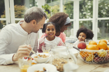 Porträt einer lächelnden multiethnischen jungen Familie beim Frühstück am Tisch - CAIF05714
