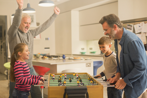 Männliche schwule Eltern und Kinder spielen Tischfußball, lizenzfreies Stockfoto