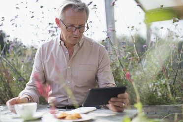 Älterer Mann, der ein digitales Tablet benutzt und am Terrassentisch Kaffee trinkt - CAIF05739