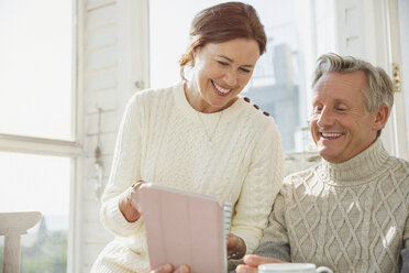 Smiling mature couple using digital tablet on sunny porch - CAIF05747