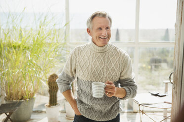 Smiling mature man drinking coffee on sunny beach house sun porch - CAIF05750