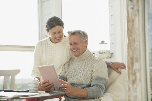 Lächelndes reifes Paar, das ein digitales Tablet am Tisch auf einer sonnigen Veranda benutzt - CAIF05751