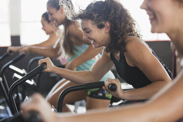 Smiling young woman using elliptical bike in exercise class - CAIF05769