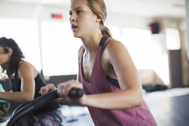 Entschlossene junge Frau auf einem elliptischen Fahrrad im Fitnessstudio - CAIF05780