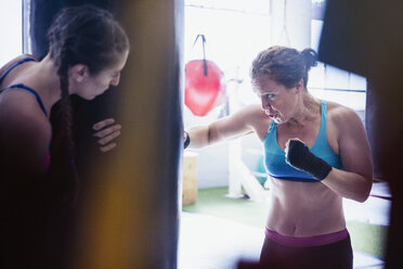 Determined, tough female boxers boxing at punching bag in gym - CAIF05781