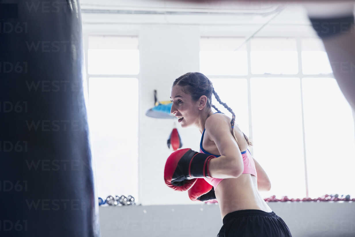 Determined, tough young female boxer shadowboxing in gym