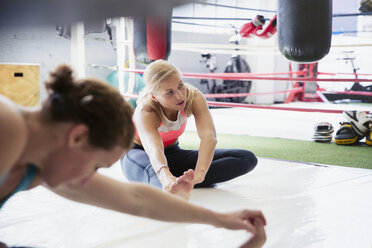 Junge Frauen strecken ihre Beine neben einem Boxring im Fitnessstudio - CAIF05794