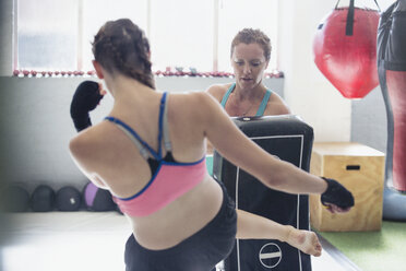 Weibliche Boxerinnen beim Kickboxen mit Polstern in der Turnhalle - CAIF05796