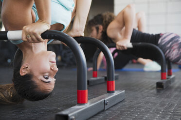 Konzentrierte junge Frau im Schulterstand an einem Gerät im Fitnessstudio - CAIF05798