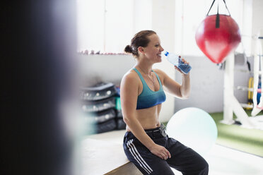 Weiblicher Boxer trinkt Wasser und ruht sich nach dem Training im Fitnessstudio aus - CAIF05805