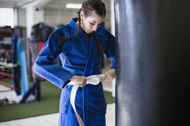 Junge Frau spannt Judogürtel am Boxsack im Fitnessstudio - CAIF05808